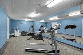Edmonton apartment for rent - A well-equipped fitness center here at Madison Park with blue accent walls, mirrored panels, and carpeted flooring. The room features treadmills, stationary exercise bikes, and cardio equipment arranged for easy movement, while overhead lighting and wall mirrors create a bright, functional space for daily workouts.