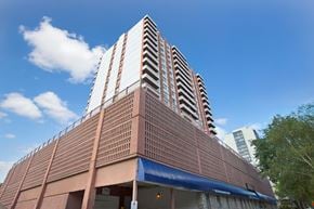Saskatoon apartment for rent - A modern high-rise apartment building here at Madison Park showcasing a distinctive architectural design with stacked balconies, a textured exterior facade, and a prominent podium level below the residential towers, set against a bright blue sky with scattered clouds and surrounding greenery.