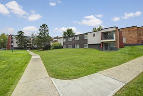 Edmonton apartment for rent - A spacious and well maintained outdoor courtyard here at Park Place South featuring expansive green lawns, curved concrete walking paths, mature trees, and multi level apartment buildings with balconies under a bright blue sky, creating a welcoming and walkable residential community setting.
