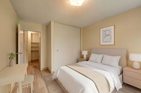 Edmonton apartment for rent - A cozy, modern bedroom here at Park Place South featuring a neatly made bed with soft neutral bedding, matching bedside tables with lamps, warm wood-style flooring, and a large closet, with light walls and simple decor creating a calm, comfortable space for rest and everyday living.
