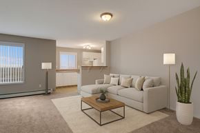 Calgary apartment for rent - A bright, spacious living room here at The Pointe at Applewood with beige carpet, a light neutral sectional sofa, and a wooden coffee table. A large window brings in natural light, with an open kitchen and breakfast bar nearby.