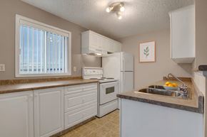Calgary apartment for rent - A bright kitchen here at Pointe at Applewood with white cabinets, brown countertops, and a double stainless steel sink. A window with vertical blinds brings in natural light, with a full appliance set and a clean, inviting layout.