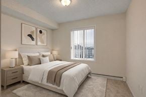 Calgary apartment for rent - A cozy bedroom here at Pointe at Applewood with beige carpet, soft neutral walls, and a large window with vertical blinds. A full bed with white bedding and bedside tables creates a warm, inviting, and relaxing atmosphere.