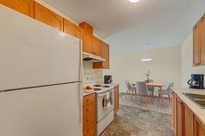 White Court apartment for rent - A functional, open kitchen here at Sol Terrace showcasing warm wood cabinetry, white appliances, and ample counter space that leads into a dedicated dining area with a light wood table, upholstered chairs, simple pendant lighting, and neutral flooring that creates a clean, welcoming atmosphere.