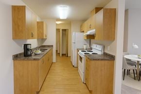 Stony Plain apartment for rent - A warm, functional kitchen here at Sonora showcasing light wood cabinetry, laminate countertops, white appliances including a refrigerator and electric range, wood-style flooring, ample storage, and a galley-style layout that opens conveniently toward the adjacent dining area.