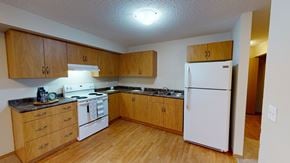 Stony Plain apartment for rent - A bright, spacious kitchen here at Sonora featuring warm wood cabinetry, durable laminate countertops, white appliances including a full-size refrigerator and electric range, wood-style flooring, generous counter space, and an open layout that offers easy access to the adjoining hallway and living areas.