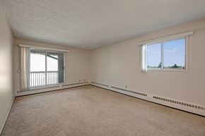 Edmonton apartment for rent - A spacious living room here at Stirling Place featuring soft carpet flooring, neutral wall tones, and a bright layout with a large sliding glass door leading to a private balcony, complemented by an additional window that brings in natural light and offers an open, comfortable space for everyday living and entertaining.