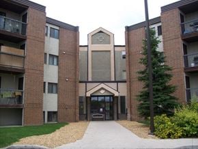 Saskatoon apartment for rent - A welcoming apartment building exterior here at Ventana showcasing a multi-story brick and neutral-tone façade, a central covered entrance with glass doors, private balcony railings on each level, landscaped walkways, and mature greenery that create a well-maintained and inviting community setting.