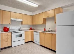 Winnipeg apartment for rent - A clean and functional kitchen here at Villagio featuring light wood cabinetry, white appliances including a refrigerator, stove, and dishwasher, ample countertop space, neutral flooring, and bright overhead lighting that creates a practical and welcoming space for everyday cooking and dining.