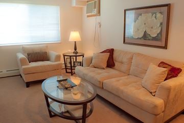 Saskatoon apartment for rent - A living room with a white couch, a glass table, and a painting on the wall.