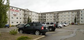 Saskatoon apartment for rent - A wide exterior view here at Wellington Manor featuring a multi-story apartment community with private balconies and a large resident parking lot. A well-kept driveway and landscaped greenery create a welcoming first impression. A clear “For Rent” sign on the building makes it easy to spot the community from the street.