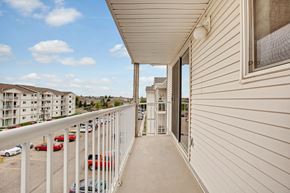 Lethbridge apartment for rent - A private balcony here at Westhaven Estates with a covered concrete patio and white railing overlooking the community grounds. A sliding glass door provides easy indoor-outdoor access and plenty of natural light. A scenic view of nearby buildings and the parking area creates an open, airy feel.