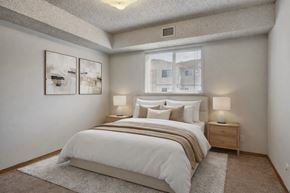 Lethbridge apartment for rent - A relaxing bedroom here at Westhaven Estates with soft carpet flooring, a cozy bed with neutral bedding, and matching nightstands with lamps. A wide window with blinds brings in natural light and adds an airy feel to the space. A simple abstract wall art set and a plush area rug create a calm and comfortable vibe.