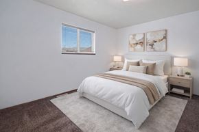 Dawson Creek apartment for rent - A bright and simple bedroom here at Willowview Terrace featuring a neatly made bed with crisp white bedding, neutral accent pillows, and a soft throw blanket. Matching nightstands with modern lamps sit on each side, with minimal decor and two framed abstract art pieces above the headboard. A large window and plush carpet help create a cozy, inviting space.
