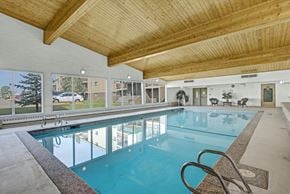 Edmonton apartment for rent - A bright indoor swimming pool here at Wyndham Crossing with clear blue water, a wide deck area, and stainless steel handrails for easy access. Large windows line the wall to bring in natural light, and the warm wood-beam ceiling adds a welcoming touch to the space.