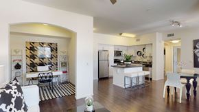 Corona apartment for rent - A bright, open-concept living space here at Artisan at Main Street Metro showcasing dark wood flooring, a modern kitchen with white cabinetry and a central island with bar seating, an adjacent dining area, and a stylish home office nook framed by an arched opening, creating a cohesive and contemporary layout ideal for everyday living.