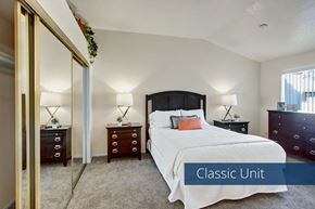 San Bernardino apartment for rent - A classic bedroom here at Castlepark with plush beige carpet, neutral walls, and a neatly made bed flanked by matching nightstands and lamps. Mirrored sliding closet doors reflect light and add storage, while a window with vertical blinds brings in natural light, creating a calm and comfortable sleeping space.