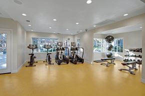 San Bernardino apartment for rent - A modern fitness center here at Castlepark with open floor space, bright overhead lighting, and large windows that let in natural light. Cardio machines line one side of the room, while a weight bench, free weights, and exercise equipment are arranged neatly, creating a clean, welcoming workout environment.