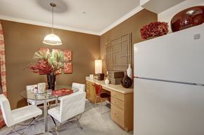 Moreno Valley apartment for rent - A cozy dining area here at Fresco with plush carpet, warm accent walls, and a round glass dining table paired with upholstered chairs. A hanging light fixture provides soft illumination, while a built-in desk with wood cabinetry adds functionality. The space connects seamlessly to the kitchen, creating an inviting area for dining and everyday tasks.