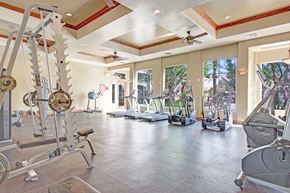 Moreno Valley apartment for rent - A spacious fitness center here at Rancho Belago featuring cardio machines and strength-training equipment arranged across an open floor plan. Large windows line the walls, allowing natural light to fill the room, while high ceilings with ceiling fans, recessed lighting, and wood-accent details create a bright and motivating workout environment.