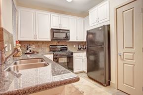 Moreno Valley apartment for rent - A well-appointed kitchen here at Rancho Belago featuring white shaker-style cabinetry, a stone-look backsplash, dark countertops with a double-basin sink, a built-in microwave above the range, a full-size refrigerator, and a clean, functional layout designed for everyday cooking and entertaining.