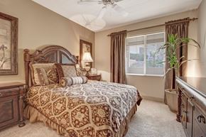 Moreno Valley apartment for rent - A warm and inviting bedroom here at Rancho Belago featuring a carved wood bed frame with layered patterned bedding, matching nightstands with soft table lamps, neutral carpet flooring, a ceiling fan, and a large window dressed with blinds and drapery that fills the space with natural light.
