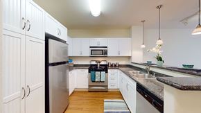 Riverside apartment for rent - A bright kitchen here at Vesada featuring white cabinetry with modern hardware, dark countertops, and stainless steel appliances arranged in a functional U-shaped layout. Pendant lighting highlights the breakfast bar, while wood-style flooring and ample counter space create an inviting setting for everyday cooking and entertaining.