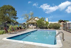 Colorado Springs apartment for rent - A bright outdoor pool here at Austin Park featuring a sparkling rectangular swimming pool with clear blue water, surrounding concrete deck with metal handrails, lounge chairs lined along the fence, and landscaped greenery, creating a refreshing community space under a sunny blue sky.