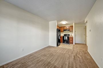 Colorado Springs apartment for rent - A room with a carpeted floor and a kitchen area in the background.