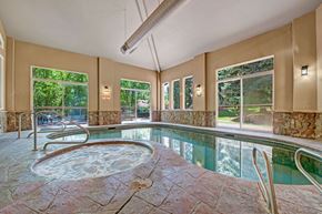 Colorado Springs apartment for rent - A bright indoor pool here at Cheyenne Creek Luxury featuring a connected spa with bubbling water, stone-accent pool deck, metal handrails for easy entry, large windows that fill the space with natural light, and peaceful views of surrounding trees creating a relaxing, resort-style atmosphere.