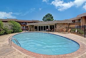 Colorado Springs apartment for rent - A refreshing outdoor pool here at Copper Stone featuring a curved swimming pool with clear blue water, surrounding concrete deck space, lounge chairs for relaxing, and a stone-accented pool house, all set within a landscaped courtyard under open skies.
