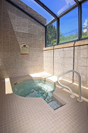 Colorado Springs apartment for rent - A bright indoor spa area here at Eagle Ridge featuring a tiled hot tub with gently bubbling water, a built-in handrail for easy access, neutral tile walls and flooring, and large angled windows overhead that allow abundant natural light and views of greenery outside.