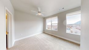 Colorado Springs apartment for rent - A spacious bedroom here at Experience at Epicenter featuring plush carpet, soft neutral walls, and a ceiling fan centered overhead. Two large windows with simple shades bring in natural light and showcase city and mountain views, while the open layout provides flexible space for a bed, nightstands, and additional furniture.