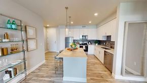 Colorado Springs apartment for rent - A contemporary kitchen here at Experience at Epicenter showcasing gray shaker-style cabinetry, stainless-steel appliances, a white quartz island with a decorative centerpiece, pendant lighting, a hexagon tile backsplash, recessed ceiling lights, and warm wood-style flooring that creates a clean, modern, and inviting cooking space.