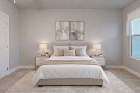 Colorado Springs apartment for rent - A serene bedroom here at Experience at Epicenter featuring plush carpet, soft neutral walls, and a centered upholstered bed dressed in layered white and beige bedding. Matching nightstands with table lamps frame the bed beneath modern wall art, while a window with simple shades allows natural light to brighten the calm, inviting space.