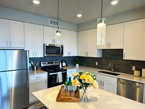 Colorado Springs apartment for rent - A modern kitchen here at Experience at Epicenter featuring white cabinetry, stainless steel appliances, a large island with quartz countertops, pendant lighting, and wood-style flooring.