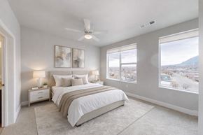 Colorado Springs apartment for rent - A bright bedroom here at Experience at Epicenter featuring a made bed with white linens, a ceiling fan, nightstands, plush carpeting, and large windows.