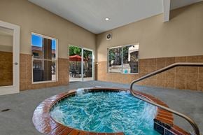 Colorado Springs apartment for rent - A relaxing indoor spa area here at Grand View featuring a circular bubbling hot tub with brick trim, clear blue water, and a metal handrail, surrounded by neutral tile flooring, large windows overlooking the outdoor patio, and warm beige walls that create a calm, comfortable retreat for residents year-round.