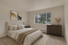 Colorado Springs apartment for rent - A bright, spacious bedroom here at Hyde Park Apartments with beige carpet, soft neutral walls, and a large window that brings in natural light and views of mature trees. The room features a comfortable bed with layered neutral bedding, a dresser, simple wall art, and a clean, calm layout that feels warm and inviting.