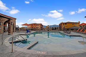 Colorado Springs apartment for rent - A scenic resort-style swimming pool here at La Bella Vita featuring clear water, built-in steps, and surrounding lounge chairs with umbrellas. A spacious stone pool deck overlooks Mediterranean-inspired buildings and distant mountain views, creating a relaxing outdoor amenity space for residents to enjoy year-round.