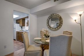 Colorado Springs apartment for rent - A warm and inviting dining area here at Windtree featuring a round glass-top dining table with upholstered chairs, soft carpet flooring, and a decorative wall mirror accented with subtle lighting, positioned just off the kitchen to create an open, comfortable space ideal for everyday meals and casual entertaining.