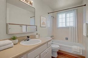 Colorado Springs apartment for rent - A bright, clean bathroom here at Yorkshire Square featuring a long vanity with a wide mirror and single sink, light cabinetry with ample storage, neutral countertops, a tub and shower combination with tiled surround, a window with vertical blinds for natural light, and warm flooring that adds contrast and comfort.