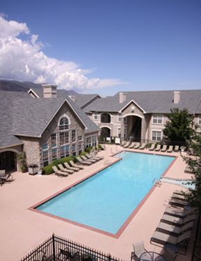 Colorado Springs apartment for rent - A resort-style outdoor pool here at Camelback Pointe featuring a long rectangular swimming pool surrounded by lounge chairs, light-colored pool decking, and elegant apartment buildings with stone accents, creating a relaxing community space under a bright sky with scenic mountain views in the background.