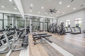 Phoenix apartment for rent - A modern fitness center here at Desert Club featuring wood-style flooring, mirrored walls, and bright overhead lighting. The space includes free weights, adjustable benches, stationary bikes, and cardio machines arranged for convenience. Large windows and glass-enclosed training areas create an open, motivating environment for daily workouts.