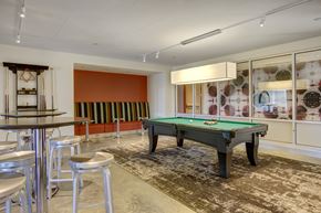 Minneapolis apartment for rent - A lively game lounge here at 7West featuring a pool table with green felt centered on a patterned area rug. High-top tables with stools sit nearby, along with built-in bench seating against a bold accent wall. Glass panels, modern lighting, and recreational cues create a social space for games and casual gatherings.
