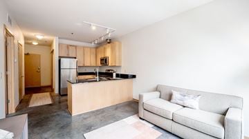 Minneapolis apartment for rent - A modern living room with a grey couch and a kitchen area in the background.