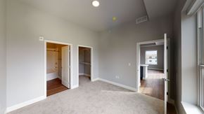 St. Paul apartment for rent - A spacious bedroom here at Collection at Highland Bridge featuring soft carpeted flooring, light gray walls, and a clean, modern layout with direct access to an en suite bathroom and a walk-in closet, complemented by recessed ceiling lighting, white trim, and an open doorway leading into the main living area with wood-style flooring.