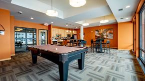 Hopkins apartment for rent - A lively community lounge here at Gallery Flats featuring a full-size pool table centered on patterned carpet flooring. High-top tables with seating, warm accent walls, and modern lighting surround the space, while large windows and glass doors bring in natural light and connect the lounge to nearby community areas.