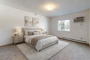 St. Cloud apartment for rent - A calm bedroom here at Heritage Park East featuring soft neutral walls, plush carpet flooring, and a large window that brings in natural light. The space includes a comfortably sized sleeping area with coordinating bedside tables and lamps, a ceiling light fixture, and an inviting layout that offers flexibility for personal furniture arrangements.