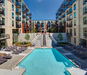 Minneapolis apartment for rent - A resort-style outdoor pool here at Inspire surrounded by modern apartment buildings with private balconies, lounge chairs, and landscaped seating areas. A wide staircase with a cascading water feature leads up through the courtyard, creating a polished, urban atmosphere designed for relaxation and social gathering.